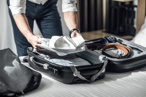 man packing his shirt into a suitcase