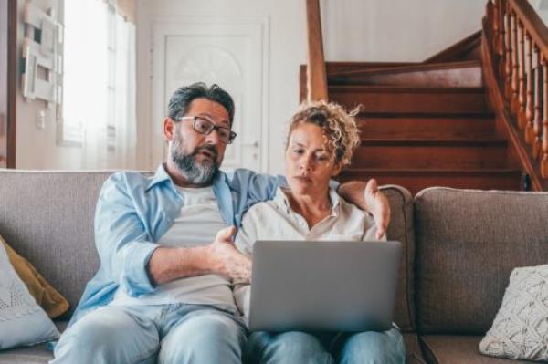 Shocked couple looking at laptop screen frustrated by unexpected bad news online. Husband and wife disappointed and feeling anxious on losing mo<em></em>ney in o<em></em>nline lottery,