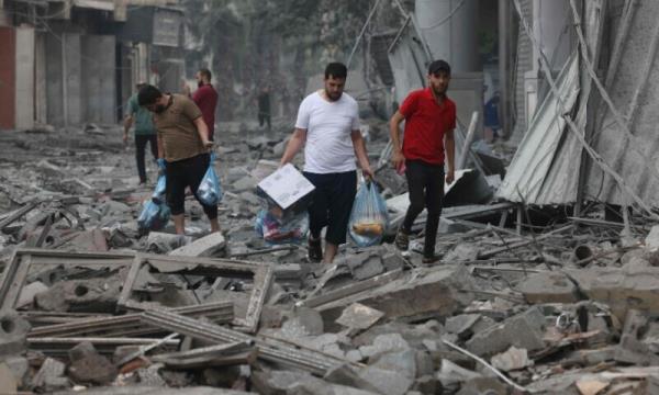 Palestinians carry food supplies as they walk through debris amid the destruction from Israeli airstrikes in Gaza City’s al-Rimal neighbourhood on October 10, 2023. — AFP